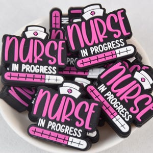 Puede incluir: Primer plano de un montón de abalorios para zapatos negros y rosas con el texto "Nurse in Progress" y un gráfico de termómetro.