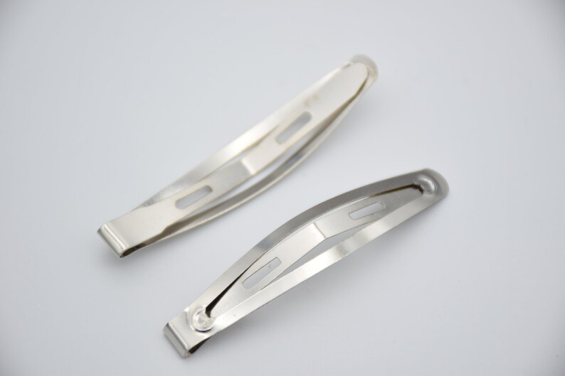 May include: Two silver metal hair clips. The clips are about 5 inches long and have a slight curve to them. They have a single hole in the center of each clip.