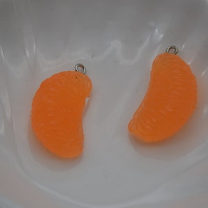 May include: Two orange, tangerine-shaped charms with silver-colored loops for jewelry making. The charms are bright orange and have a textured surface, resembling a real tangerine segment. They are set against a white background.