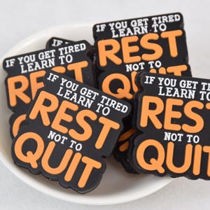 Pode incluir: Um close-up de vários patches motivacionais laranja e preto que dizem "Se você se cansar, aprenda a descansar, não a desistir".