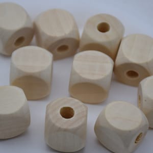以下が含まれることがあります： 未完成の木製キューブビーズのコレクション。各ビーズは自然な淡いベージュ色で、中央に円筒形の穴が開いています。これらのクラフトビーズは、ジュエリー作りやその他のDIYプロジェクトに最適です。