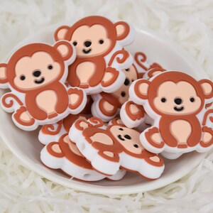 Puede incluir: Un grupo de juguetes para masticar de silicona en forma de mono, de color marrón y blanco. Los monos tienen un diseño de dibujos animados lindo con ojos grandes y una sonrisa.