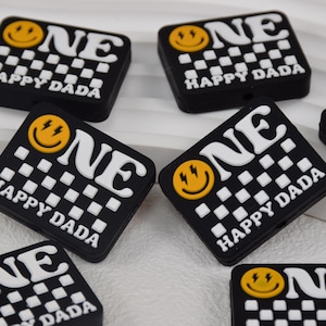 May include: Eight black and white checkerboard patterned charms with a yellow smiley face and the word "ONE" in white letters. The charms also have the text "HAPPY DADA" in white letters.