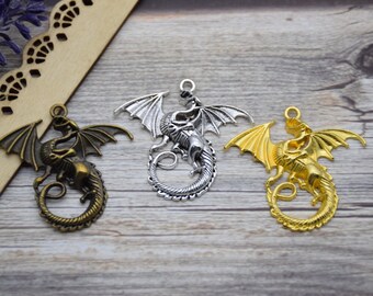 May include: Three metal dragon charms in different finishes: antique bronze, silver, and gold. Each charm features a detailed dragon design with wings outstretched and a curled tail.