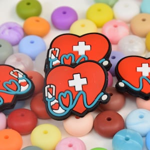 May include: Three red heart-shaped silicone charms with a white cross and a blue stethoscope design. The charms are surrounded by colorful silicone beads.
