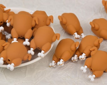 May include: A selection of small, brown turkey charms with white leg details. The charms are arranged on a white surface and in a white dish. These charms are likely used for crafting or jewellery making.
