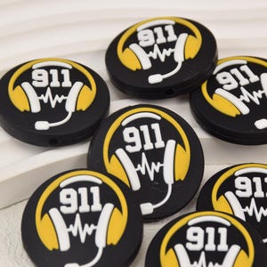 May include: Six black silicone charms with a yellow headphone design and the text "911" in white. Each charm has a small hole for attaching to a necklace or bracelet.