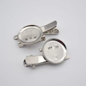 May include: Two silver-toned metal brooch backs with a round, flat surface and a clip on the back.
