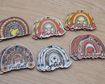 Könnte beinhalten: Holzornamente in Regenbogenform mit Sportmotiven. Designs umfassen Baseball, Softball, Basketball, American Football und Fußball, mit dekorativen Elementen und Text. Jedes Ornament hat ein kleines Loch zum Aufhängen.