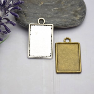 May include: Two blank metal pendant charms, one silver and one bronze, with a rectangular shape and a loop at the top for hanging.