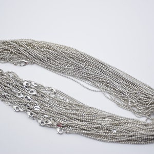 May include: A pile of silver ball chain necklaces, each with a lobster clasp closure.