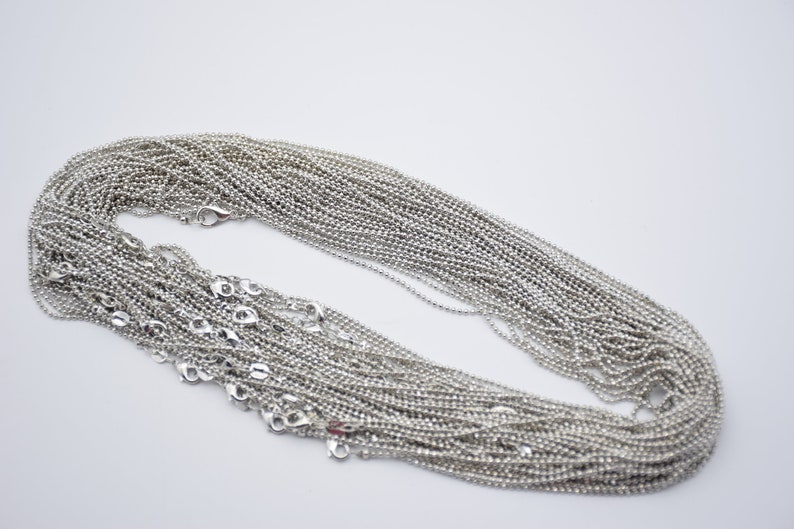 May include: A pile of silver ball chain necklaces, each with a lobster clasp closure.