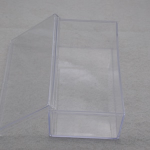 May include: A clear plastic box with a hinged lid. The box is empty and has a rectangular shape.