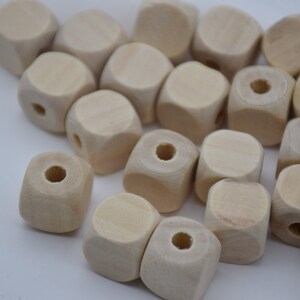 以下が含まれることがあります： 未完成の木製ビーズのコレクション。ビーズは立方体で、角が丸く、中央に穴が開いています。天然木のカラーはライトベージュです。これらのビーズは、さまざまなクラフトプロジェクトに適しています。