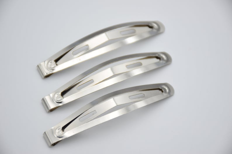 May include: Three silver metal hair clips, each with a curved shape and two small holes. The clips are stacked on top of each other.