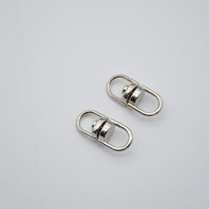 May include: Two silver swivel clasps with a round metal loop on each end. The clasps are designed to attach to a strap or chain.