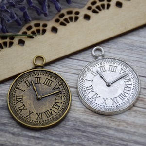 Könnte beinhalten: Zwei antike Uhren-Anhänger, einer in Silber und einer in Bronze, mit römischen Ziffern und einem detaillierten Design.