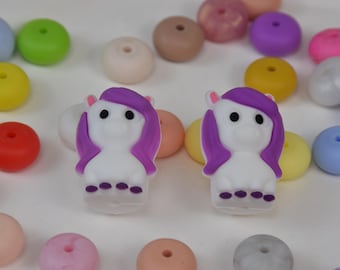 May include: Two white unicorn-shaped beads with purple manes and tails, surrounded by colorful round beads in various shades. The beads are in shades of pink, purple, yellow, blue, and orange. These beads are likely for crafting or jewelry making.