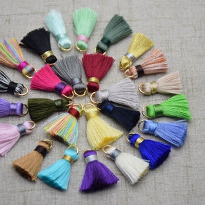 May include: A collection of 20 colorful tassel charms with gold rings. The tassels are made of various colors, including pink, blue, green, purple, yellow, and red.