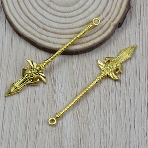 K&ouml;nnte beinhalten: Zwei goldfarbene Speer-Anh&auml;nger mit aufwendigen Details. Jeder Anh&auml;nger hat ein verziertes Speerkopf-Design und einen strukturierten Schaft. Die Anh&auml;nger haben oben eine Schlaufe zur einfachen Befestigung, ideal f&uuml;r Schmuckherstellung oder Bastelprojekte.
