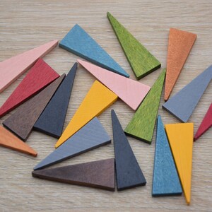 May include: A collection of 15 wooden triangular pieces in various colours, including red, blue, green, yellow, orange, pink, and brown. The pieces are arranged in a random pattern on a light wood surface.