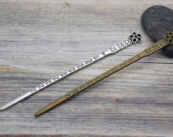 Può includere: Due bastoncini per capelli decorativi con motivi floreali decorati. Un bastoncino è argentato con dettagli neri, l'altro è dorato con dettagli neri.