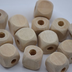 以下が含まれることがあります： 未完成の木製キューブビーズのコレクション。各キューブには、中央に穴と、紐を通すのに最適な小さな穴が側面にあります。ビーズのサイズは約2.5cmです。