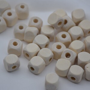 以下が含まれることがあります： 小さな未完成の木製キューブビーズのコレクション。各キューブは丸みを帯びたエッジと中央に穴が開いており、紐を通すのに最適です。ビーズは自然な淡いベージュ色です。