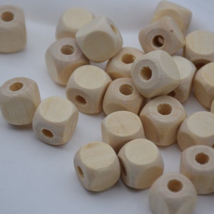 May include: A pile of natural wood cube beads with a hole through the center of each bead. The beads are unfinished and ready to be painted or stained.