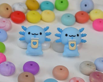 Puede incluir: Dos figuras de ajolote azul claro, cada una sosteniendo una taza de café con un diseño de corazón. Las figuras están rodeadas de cuentas redondas y coloridas en tonos rosa, amarillo, azul y verde. Los ajolotes tienen una apariencia linda y de dibujos animados.