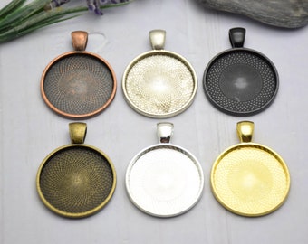 May include: Six round metal pendant trays with different finishes. The trays are silver, gold, black, copper, and two shades of bronze. Each tray has a raised edge and a loop for hanging.