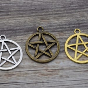 Puede incluir: Tres dijes de pentagrama en plata, bronce y oro con un diseño de estrella de cinco puntas. Los dijes son redondos y tienen un bucle en la parte superior para colgar.