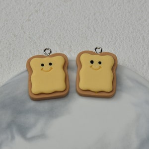 May include: Two brown and yellow smiling toast charms with silver jump rings.