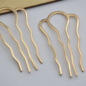 Op de afbeelding: Twee gouden haar kammen met een golvend ontwerp. De kammen hebben elk drie tanden.