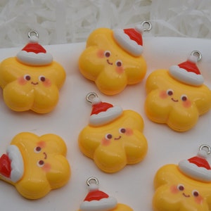 Könnte beinhalten: Sechs gelbe sternförmige Charms mit roten und weißen Weihnachtsmützen. Jeder Charm hat ein fröhliches Gesicht mit rosigen Wangen und eine silberne Schlaufe zum Aufhängen.