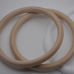 May include: Two wooden rings, one slightly larger than the other, are stacked on top of each other. The rings are a light beige color and have a smooth, polished finish.