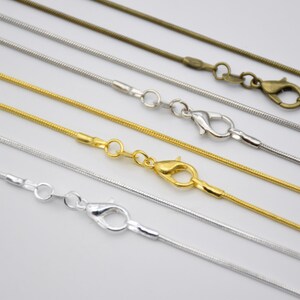 Op de afbeelding: Vijf verschillende slangenkettingen in zilver, goud en brons met karabijnhaken.