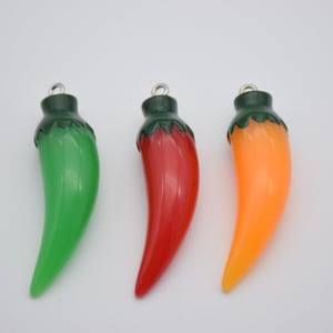 Puede incluir: Tres abalorios de chile, uno verde, uno rojo y uno naranja. Cada abalorio tiene un lazo plateado para colgar.