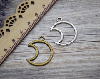 May include: Two metal crescent moon charms, one silver and one bronze, on a wooden surface.