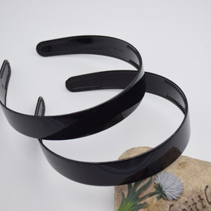 May include: Two black plastic headbands. The headbands are shiny and have a smooth surface.