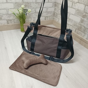 Pode incluir: Uma bolsa de transporte para animais de estimação em tons de castanho e bege, com alças pretas e detalhes em rede. Inclui uma almofada em forma de osso e uma cama retangular a condizer. A bolsa tem uma pega e uma alça de ombro.