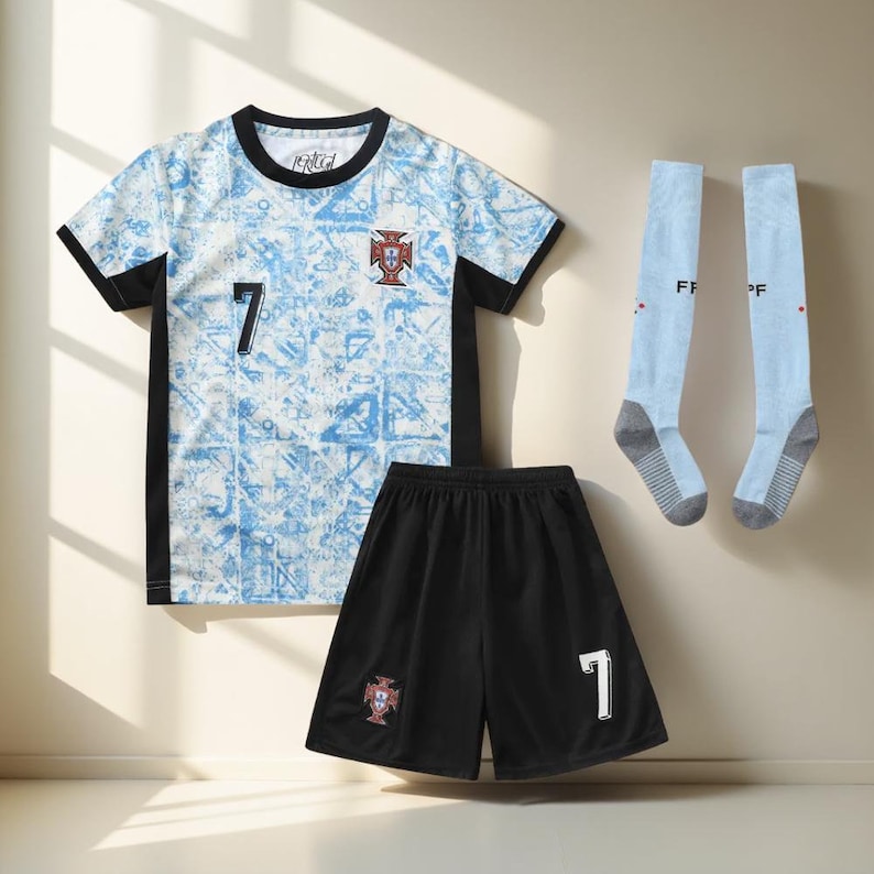 May include: A soccer uniform set in blue and black with the number 7 on the jersey and shorts. The jersey has a white and blue pattern and a red and gold crest. The shorts are black with a red and gold crest. The socks are light blue with the letters "FP" on them.