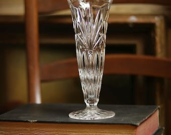 May include: A clear glass vase with a cut-glass design sits on top of two books. The books are stacked on top of each other. The top book is black with a gold spine. The bottom book is brown with a gold spine.
