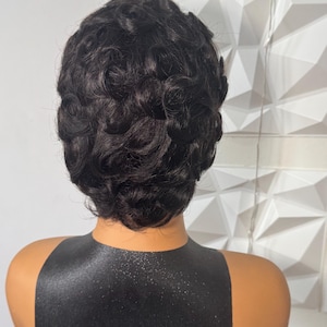 May include: A short, black wig with tight, defined curls styled in a pixie cut. The hair has a glossy finish and is arranged in uniform, circular patterns covering the entire head, creating a textured, voluminous look on a mannequin.