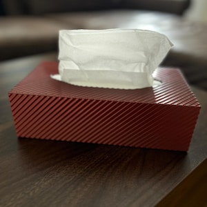 May include: A red tissue box with a white tissue pulled out. The tissue box has a striped pattern.