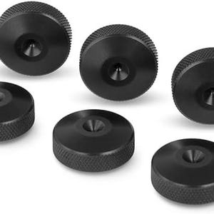 Könnte beinhalten: Ein Set aus sieben runden schwarzen Metallknöpfen mit gerändeltem Rand und einer zentralen konischen Vertiefung. Jeder Knopf hat eine flache Oberseite und einen zylindrischen Körper, die in einer verstreuten Formation angeordnet sind.