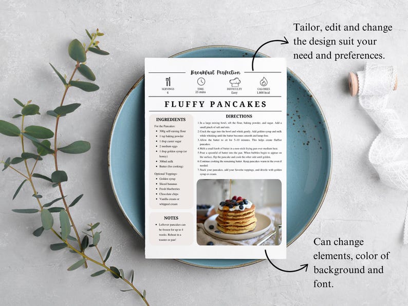 K&ouml;nnte beinhalten: Eine Rezeptkarte f&uuml;r fluffige Pfannkuchen liegt auf einem blauen Teller, mit einem Zweig Gr&uuml;n und einer Rolle wei&szlig;em Band. Die Karte enth&auml;lt eine Zutatenliste und Anweisungen sowie ein Foto von Pfannkuchen mit Beeren. Der Text auf der Karte lautet "Fluffy Pancakes".