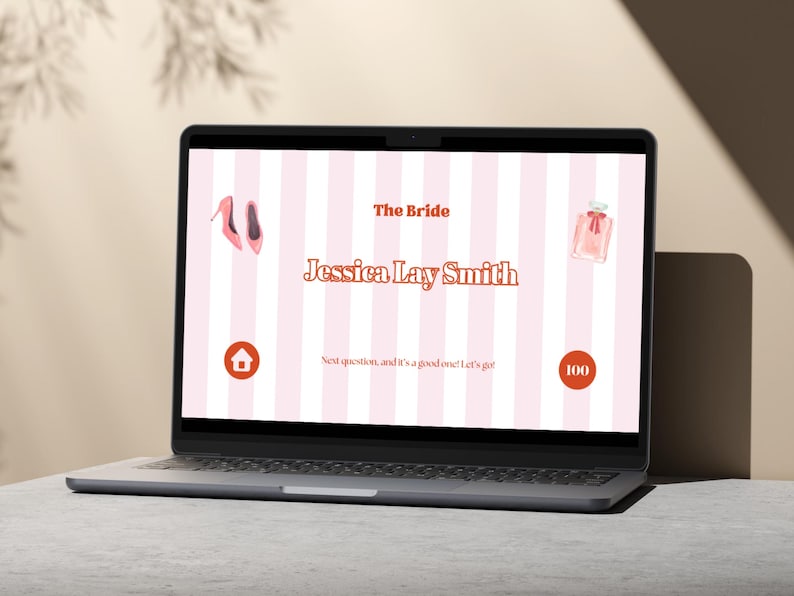 May include: A laptop screen displaying a pink and white striped background with the text "The Bride Jessica Lay Smith" in orange. The screen also shows a pink shoe, a pink perfume bottle, a red house icon, and a red circle with the number 100 inside.