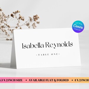 May include: A white folded place card featuring the black printed name Isabella Reynolds and the text TABLE ONE. The card is available in 8.89 x 5.08 cm or 10.16 x 5.08 cm sizes. A circular blue and purple badge with the text EDIT WITH CANVA TEMPLATE is visible.