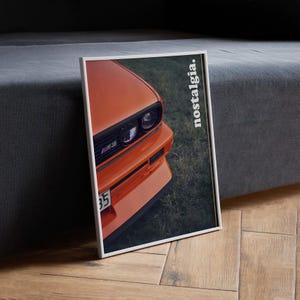 May include: A close-up of an orange car with black headlights and the word "nostalgia" printed on the side. The car is parked on a grassy surface.